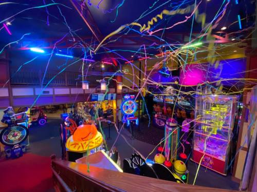 A vibrant arcade filled with colorful lights, games, and streamers hanging from the ceiling.
