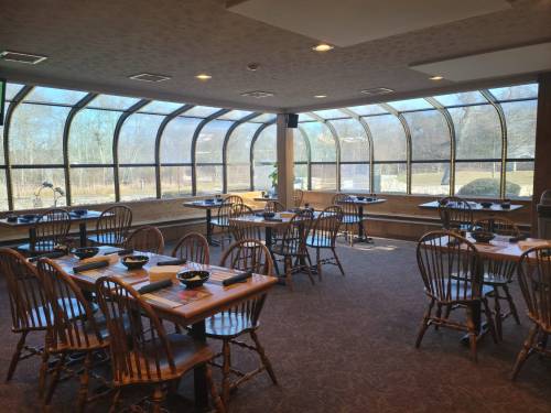 A bright restaurant interior with wooden tables and chairs, featuring large windows overlooking a scenic view.