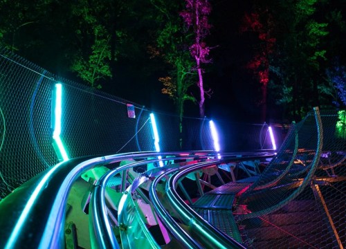 A brightly lit roller coaster track at night, surrounded by colorful neon lights and trees.