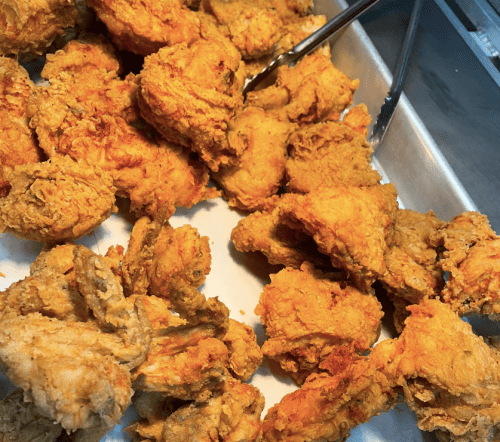 A tray of golden-brown fried chicken pieces, crispy and freshly cooked, with tongs resting on the side.