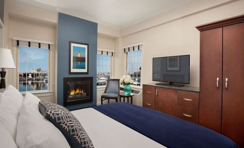 Cozy hotel room with a bed, fireplace, TV, and large windows showcasing a scenic view.