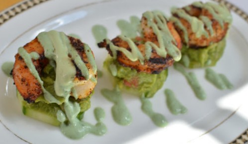 Three grilled shrimp on cucumber slices, topped with green sauce and served on a white plate.