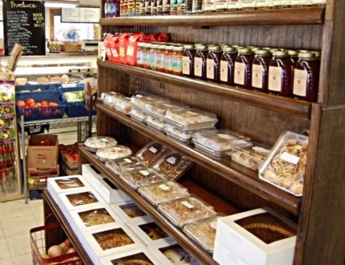 A wooden display shelf filled with jars, baked goods, and packaged treats in a cozy grocery store.