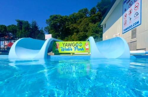 A clear blue pool with two water slides and a sign for Yawgoo Water Park in the background under a sunny sky.