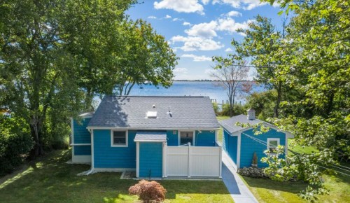 A bright blue house surrounded by trees, with a view of a lake and blue sky in the background.