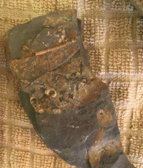 A rough, dark rock fragment with rusty patches, resting on a textured beige cloth.