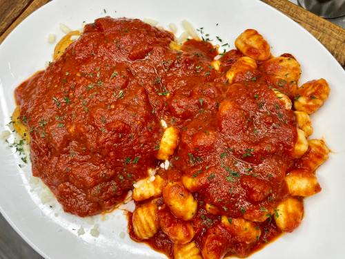 A plate of gnocchi topped with rich tomato sauce and herbs, served alongside a large meatball.