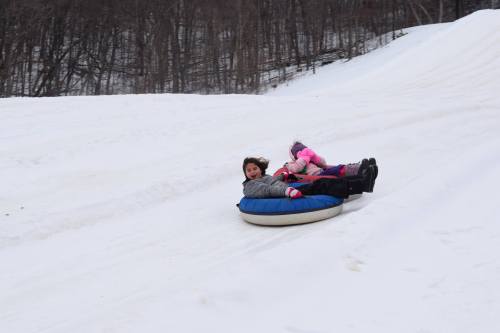 Two children slide down a snowy hill on a tube, laughing and enjoying a winter day.