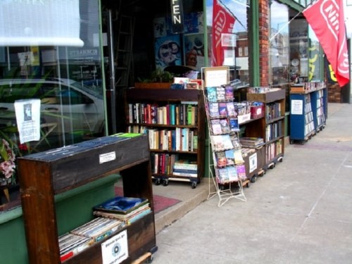 Outdoor bookshop display with wooden shelves filled with books and magazines, set along a sidewalk.