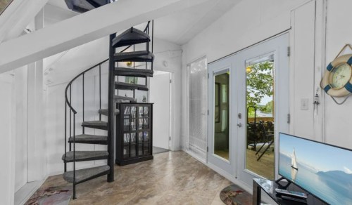 A bright, modern interior featuring a spiral staircase, large windows, and a TV, with a view of the outdoors.