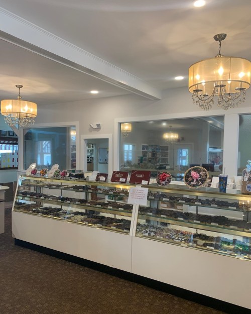 Interior of a shop featuring display cases of chocolates, elegant chandeliers, and a bright, inviting atmosphere.