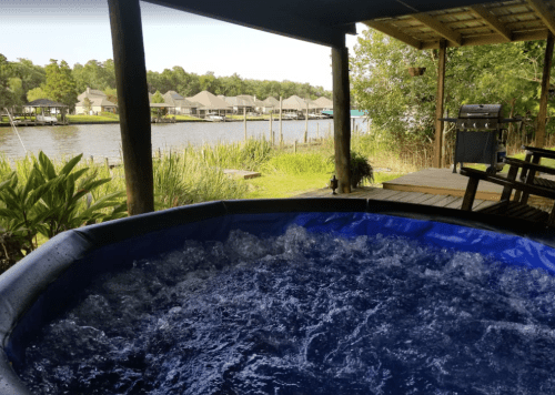 A bubbling hot tub on a deck overlooking a serene river and lush greenery.