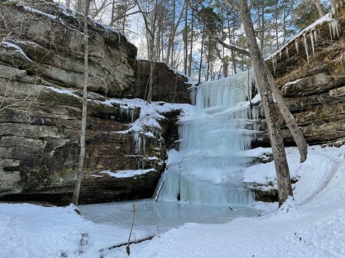 A frozen waterfall surrounded by snow-covered rocks and trees in a winter landscape.