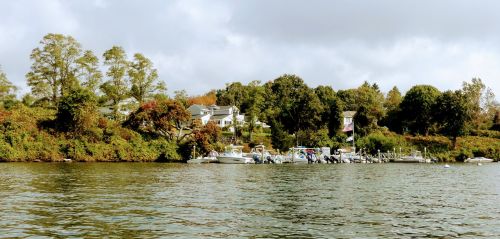 A serene lakeside view featuring boats docked near a lush, green shoreline and a house in the background.