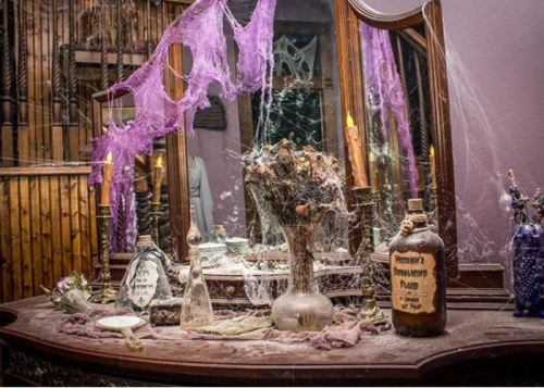A dusty vanity table adorned with cobwebs, old bottles, and a wilted flower arrangement, creating a spooky atmosphere.