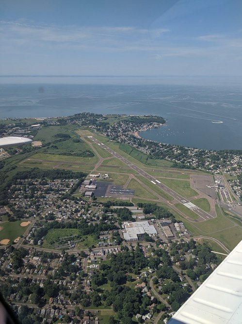 Aerial view of a coastal area featuring an airport runway, nearby buildings, and a body of water in the background.