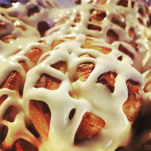 Close-up of freshly baked cinnamon rolls drizzled with creamy icing, showcasing a golden-brown, flaky texture.