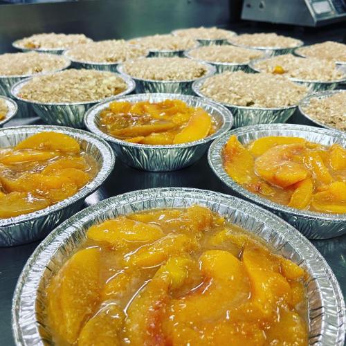 Close-up of individual dessert cups filled with peach slices and topped with oatmeal crumble, arranged on a countertop.