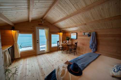 Cozy wooden room with ocean views, featuring a bed, dining table, and warm lighting.