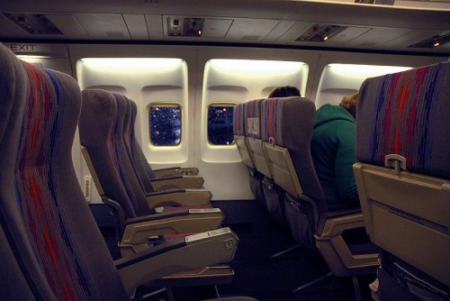 Interior of an airplane with empty seats and passengers, featuring a view of stars through the windows.