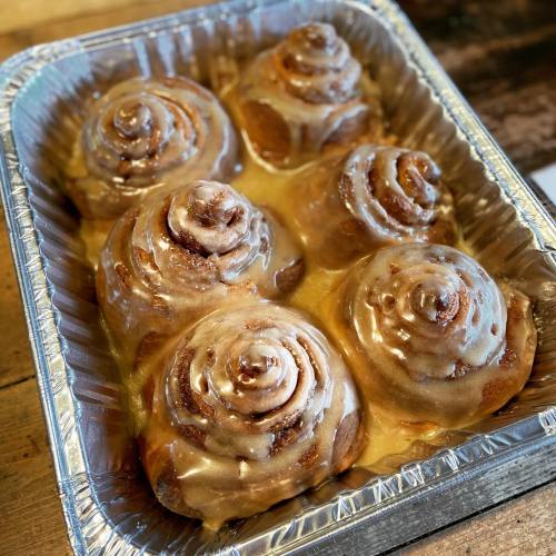 A tray of six freshly baked cinnamon rolls topped with creamy icing.