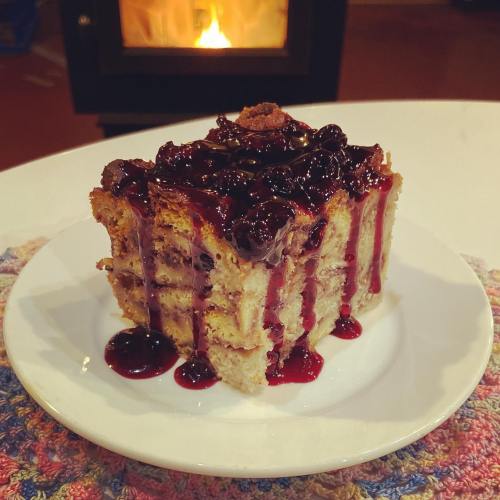 A slice of layered cake topped with cherry sauce, served on a white plate with a cozy fireplace in the background.