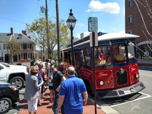 A red trolley parked on a street with people gathered around, enjoying a sunny day in a small town.