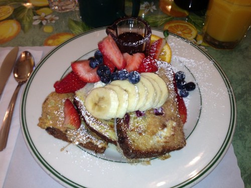A plate of French toast topped with strawberries, blueberries, banana slices, and a drizzle of chocolate sauce.