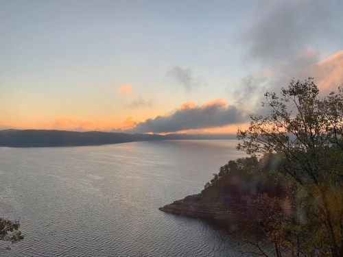 A serene lake at sunset, with soft clouds and a distant shoreline reflecting warm colors in the water.