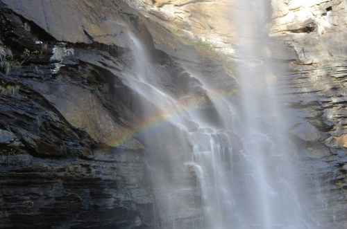 A waterfall cascading down rocky cliffs, with a faint rainbow appearing in the mist.