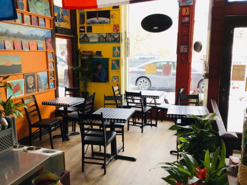Cozy café interior with colorful walls, empty tables, and plants, featuring artwork and large windows.