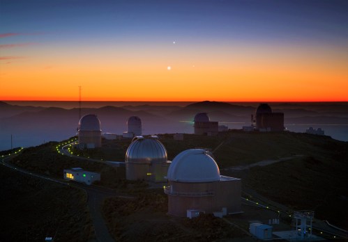 A scenic view of observatories at sunset, with a gradient sky and distant mountains.