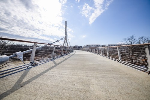 A modern pedestrian bridge stretches into the distance under a partly cloudy sky.