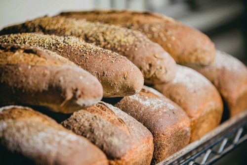 Freshly baked loaves of bread with a golden crust and sprinkled seeds, arranged on a cooling rack.