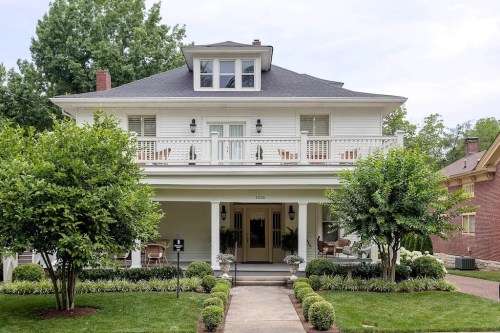 A charming two-story house with a balcony, surrounded by greenery and a well-maintained garden path.