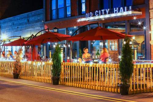 Outdoor dining area with red umbrellas and wooden fencing at Old City Hall, illuminated at night.