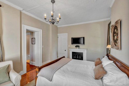 Cozy bedroom featuring a bed, chandelier, fireplace, and soft color palette with natural light.