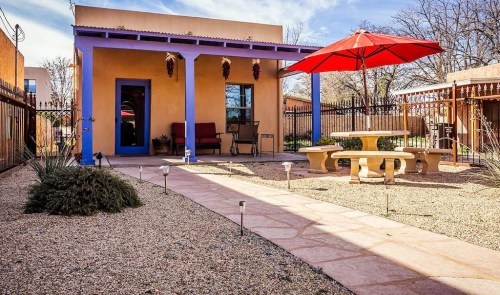 A colorful adobe-style house with a red umbrella, surrounded by a gravel garden and a stone pathway.