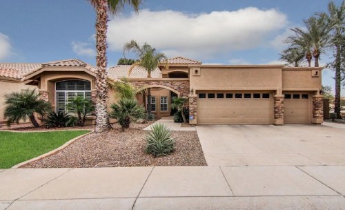A modern home with a stone facade, palm trees, and a two-car garage, set against a blue sky.