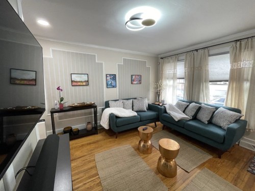 Cozy living room with teal sofas, wooden coffee tables, and decorative wall art, featuring natural light from large windows.