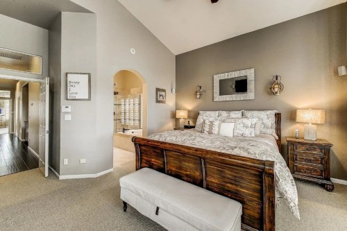 Cozy bedroom with a wooden bed, decorative pillows, nightstands, and soft lighting, featuring neutral tones and a spacious layout.
