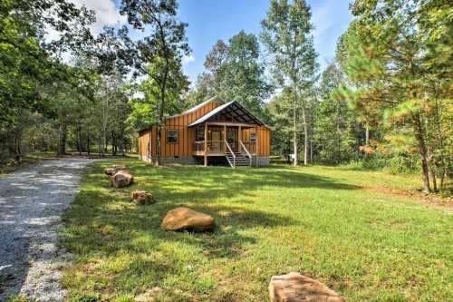 A modern cabin with a wooden exterior surrounded by trees and a gravel path in a lush green landscape.