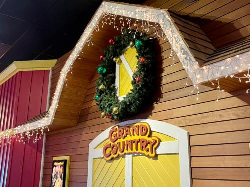A festive wooden wall with a wreath and holiday lights, featuring a sign that reads "Grand Country."
