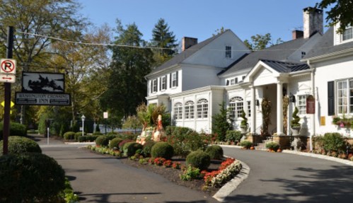 A charming white inn surrounded by colorful flowers and greenery, with a sign for Washington Crossing Inn.