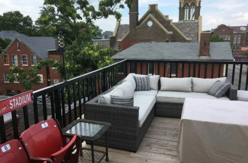 A rooftop patio with a sectional sofa, table, and views of nearby buildings and trees.
