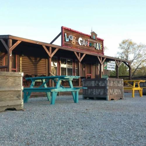 A rustic café with colorful picnic tables outside, featuring a wooden sign that reads "Log Cabin Café."