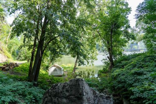 A serene campsite by a lake, surrounded by lush greenery and trees, with a tent set up near the water's edge.
