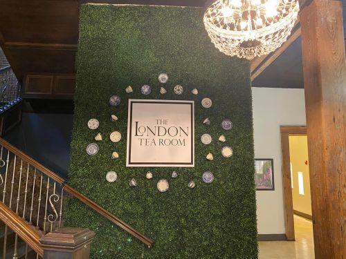 A decorative wall with greenery and plates, featuring a sign that reads "The London Tea Room." A chandelier is visible above.