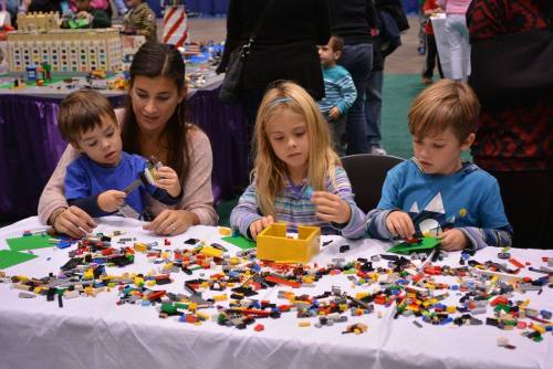 A woman and three children play with colorful LEGO bricks on a table, building and creating together.