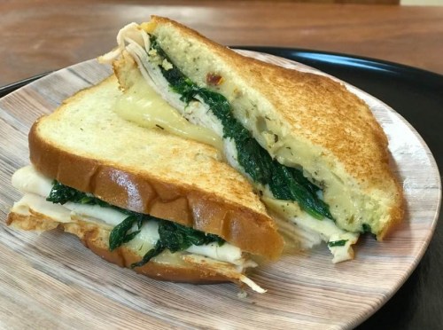 A toasted sandwich with turkey, melted cheese, and spinach, served on a wooden plate.